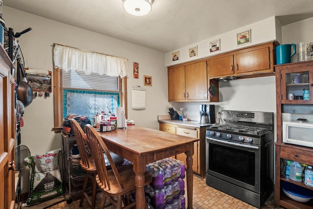 kitchen with gas range, white microwave, brown cabinets, and light countertops