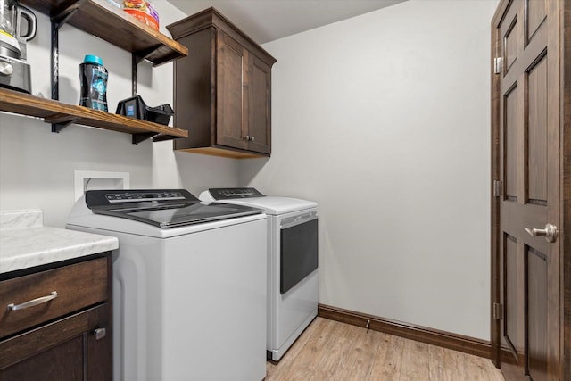 clothes washing area featuring baseboards, light wood finished floors, cabinet space, and washer and dryer