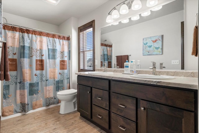 bathroom featuring wood finished floors, a sink, toilet, and double vanity