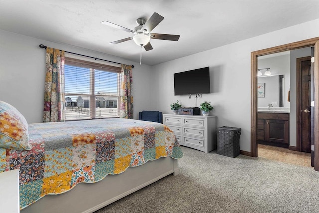 bedroom featuring light carpet, baseboards, ceiling fan, ensuite bathroom, and a sink