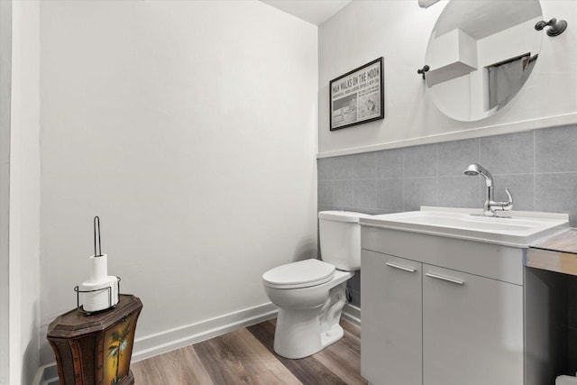 bathroom with tile walls, toilet, vanity, wood finished floors, and baseboards