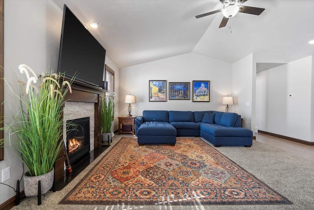 living room with a ceiling fan, vaulted ceiling, a stone fireplace, and baseboards