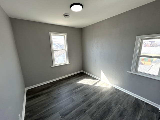 unfurnished room with visible vents, baseboards, and dark wood-style flooring