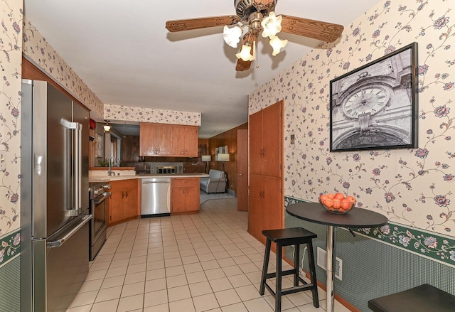 kitchen with wallpapered walls, light countertops, light tile patterned floors, brown cabinets, and stainless steel appliances