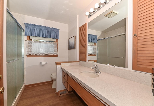 full bath featuring a shower with door, baseboards, toilet, wood finished floors, and vanity