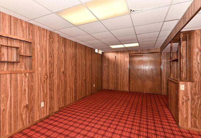 finished basement featuring a drop ceiling and wood walls