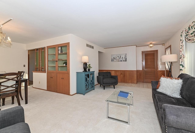 living room featuring a wainscoted wall, visible vents, wood walls, light carpet, and a notable chandelier