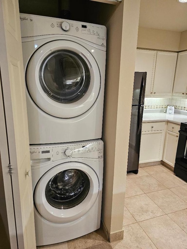 laundry area with light tile patterned floors, baseboards, laundry area, and stacked washer / dryer