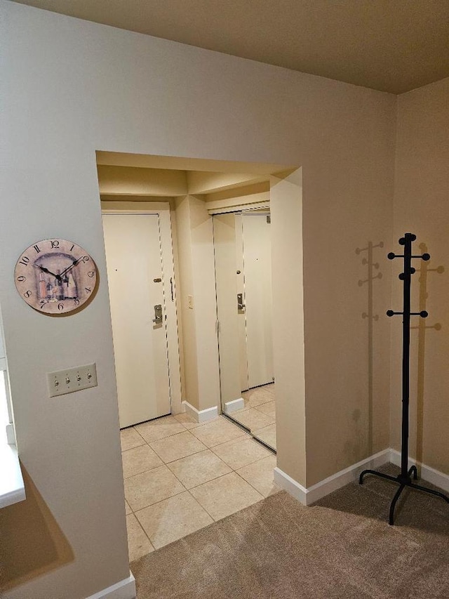 hallway featuring light tile patterned floors, light colored carpet, and baseboards