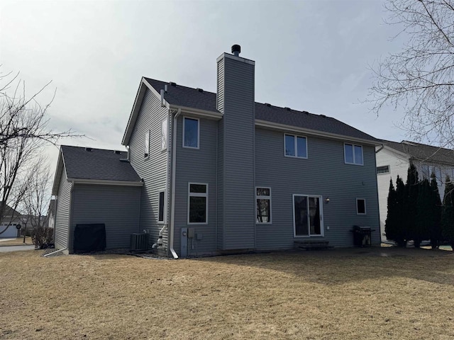 back of house featuring a yard, roof with shingles, central AC unit, and a chimney