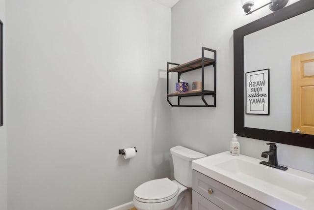 half bathroom featuring baseboards, toilet, and vanity