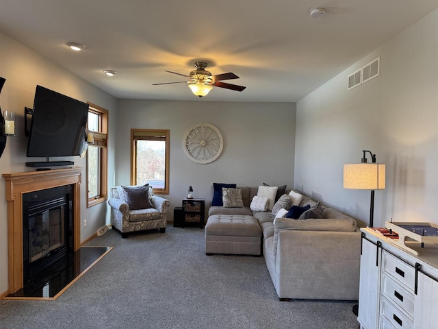 living room with visible vents, carpet flooring, a ceiling fan, and a glass covered fireplace