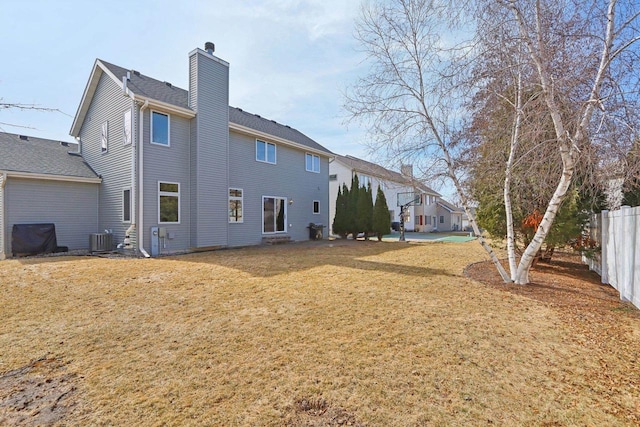 back of house featuring central AC unit, a yard, fence, and a chimney