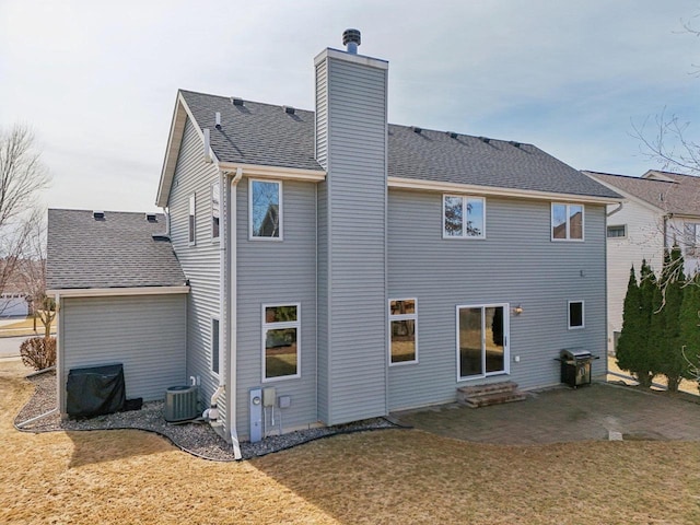 back of house featuring a patio area, a lawn, a chimney, and roof with shingles