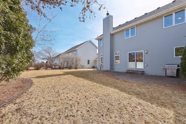 back of property featuring entry steps, a patio, a lawn, and a chimney