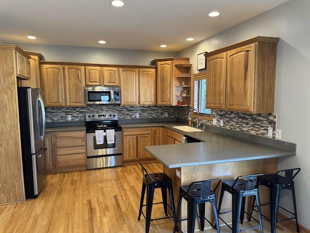 kitchen with a breakfast bar, a peninsula, open shelves, a sink, and stainless steel appliances