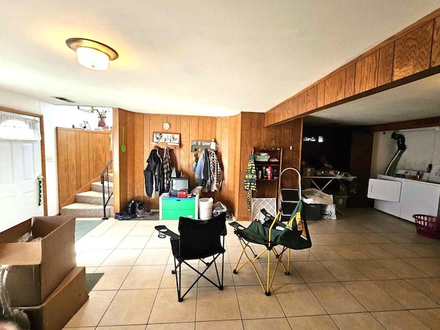 interior space with light tile patterned flooring, washing machine and dryer, wooden walls, visible vents, and stairs