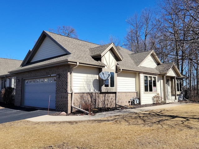 view of home's exterior with an attached garage, a shingled roof, aphalt driveway, and brick siding