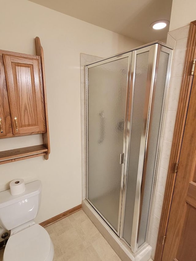 full bath featuring toilet, a stall shower, and baseboards