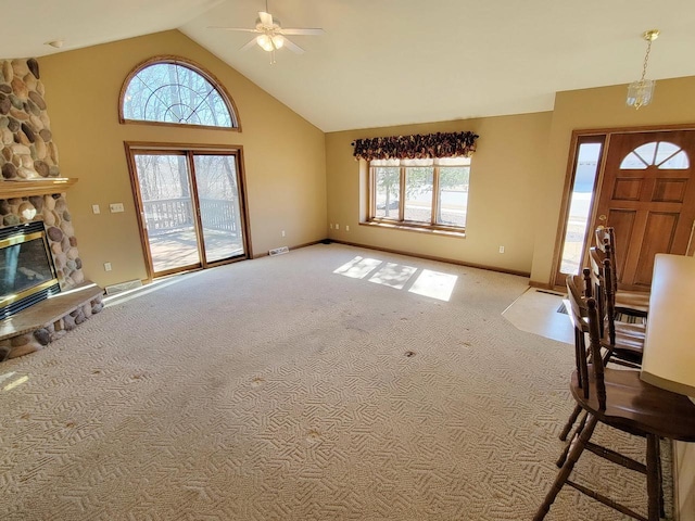 entryway featuring high vaulted ceiling, light colored carpet, a healthy amount of sunlight, and a fireplace