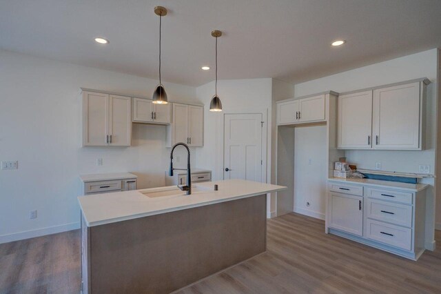 kitchen featuring light countertops, hanging light fixtures, a kitchen island with sink, a sink, and wood finished floors