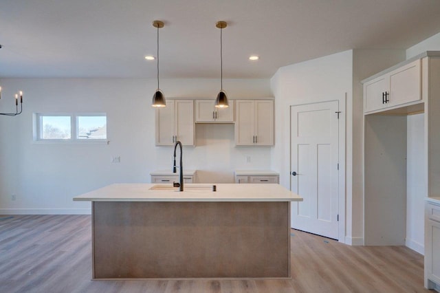 kitchen with light wood finished floors, a center island with sink, baseboards, decorative light fixtures, and a sink