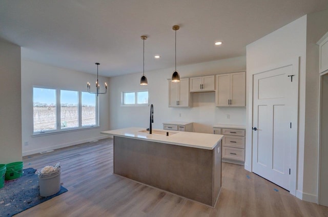 kitchen featuring an island with sink, baseboards, a sink, and wood finished floors