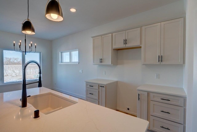 kitchen featuring a chandelier, a sink, white cabinets, and pendant lighting