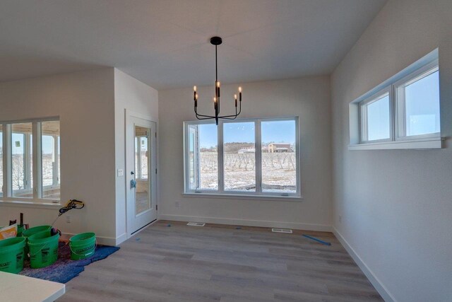 unfurnished dining area featuring wood finished floors, visible vents, baseboards, and an inviting chandelier