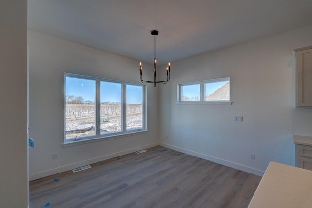 unfurnished dining area with an inviting chandelier, light wood-style flooring, visible vents, and baseboards