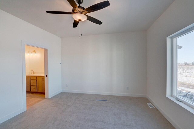 empty room with ceiling fan, light colored carpet, a sink, visible vents, and baseboards