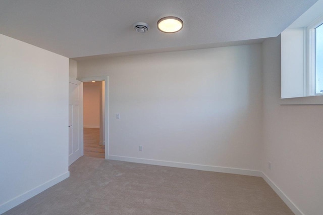 spare room featuring light carpet and baseboards