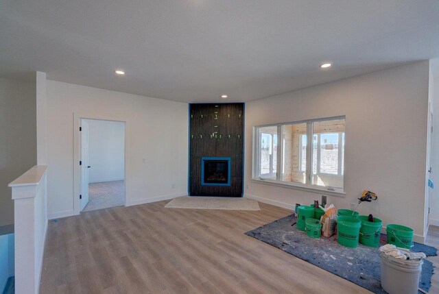 unfurnished living room featuring recessed lighting, a large fireplace, baseboards, and wood finished floors