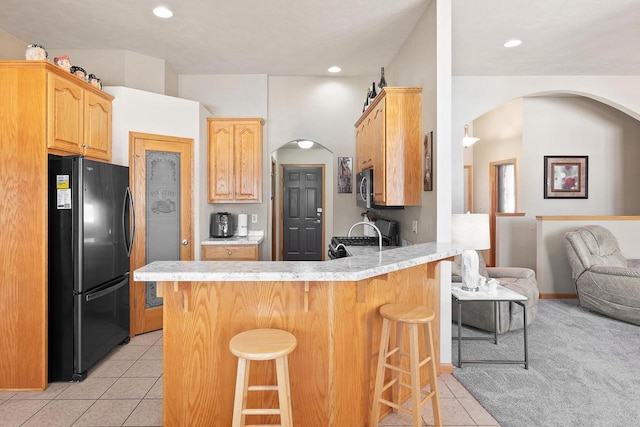 kitchen featuring light countertops, stainless steel microwave, freestanding refrigerator, light tile patterned flooring, and a peninsula