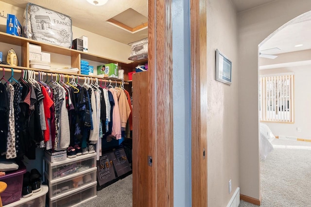 spacious closet featuring arched walkways, carpet floors, and attic access