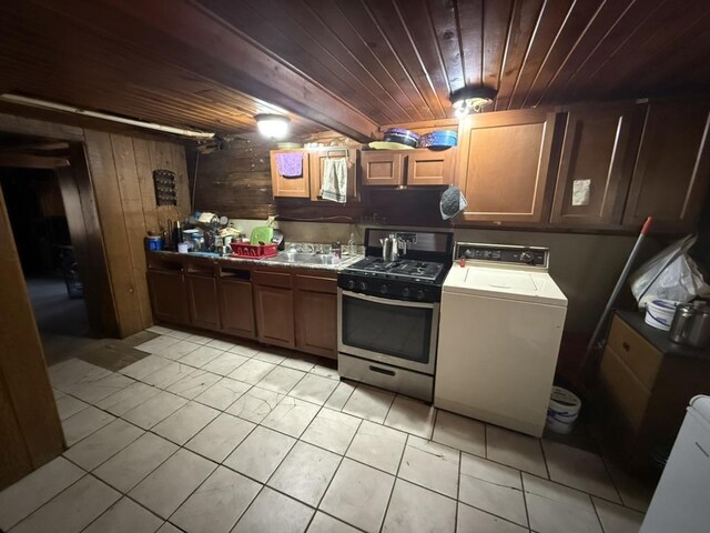 kitchen with light tile patterned floors, wood ceiling, stainless steel range with gas stovetop, wooden walls, and washer / dryer