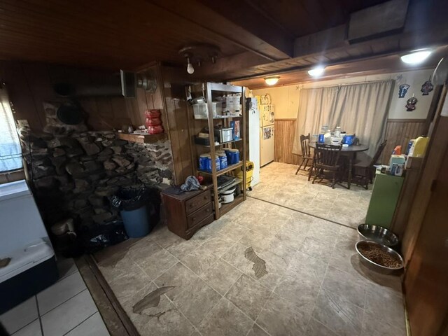 below grade area with wood walls, freestanding refrigerator, and wainscoting