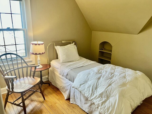 bedroom with baseboards, lofted ceiling, and wood finished floors