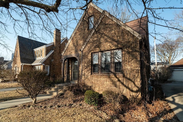 view of front facade with brick siding, a chimney, and a shingled roof