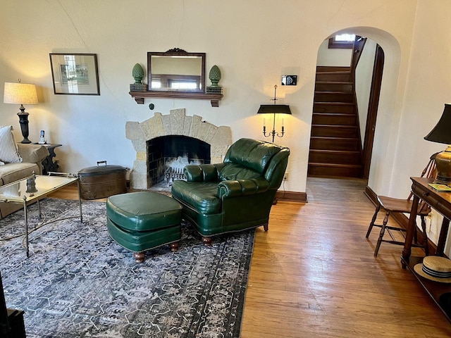 living area featuring baseboards, stairs, a fireplace, wood finished floors, and arched walkways