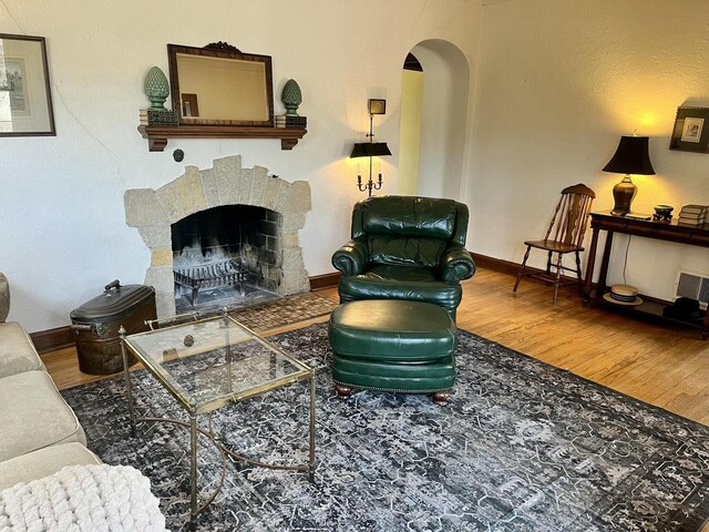 living room with arched walkways, a fireplace, baseboards, and wood finished floors