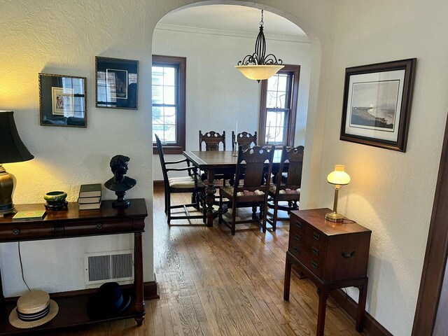 dining room with visible vents, crown molding, baseboards, hardwood / wood-style flooring, and arched walkways