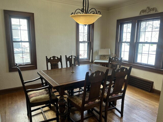 dining room with visible vents, ornamental molding, wood finished floors, baseboards, and a textured wall