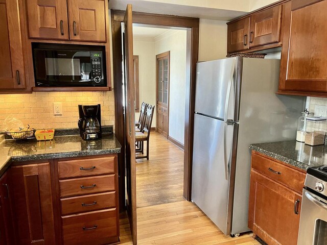 kitchen featuring light wood-style flooring, dark stone countertops, tasteful backsplash, appliances with stainless steel finishes, and crown molding