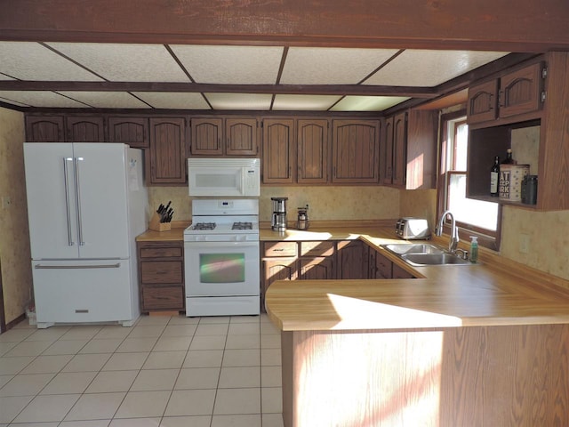 kitchen featuring light countertops, a peninsula, light tile patterned flooring, white appliances, and a sink