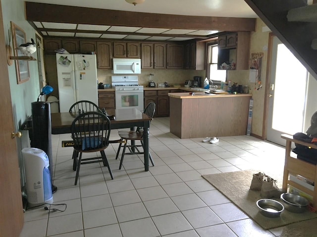 kitchen with beam ceiling, white appliances, a peninsula, light tile patterned flooring, and light countertops