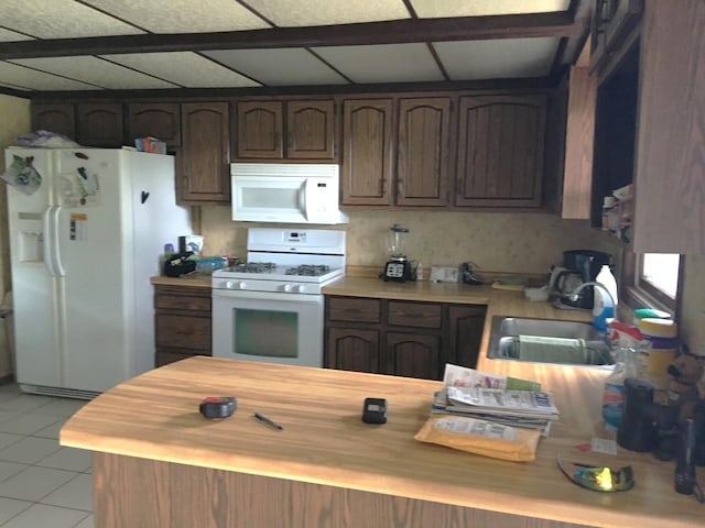 kitchen featuring white appliances, light tile patterned flooring, a drop ceiling, a sink, and dark brown cabinetry