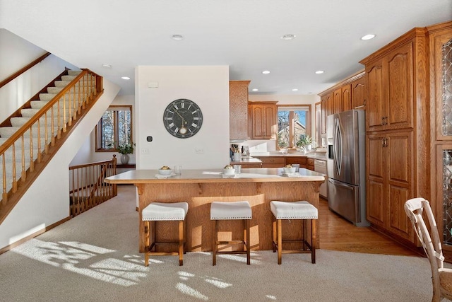 kitchen with a breakfast bar area, light countertops, stainless steel fridge with ice dispenser, and recessed lighting