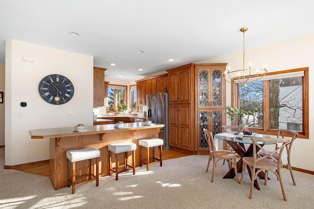 kitchen with brown cabinets, a breakfast bar area, recessed lighting, glass insert cabinets, and stainless steel fridge with ice dispenser