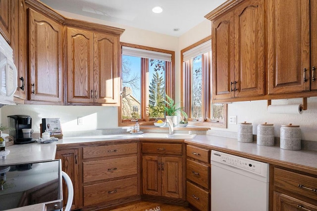 kitchen featuring brown cabinets, recessed lighting, light countertops, a sink, and white appliances